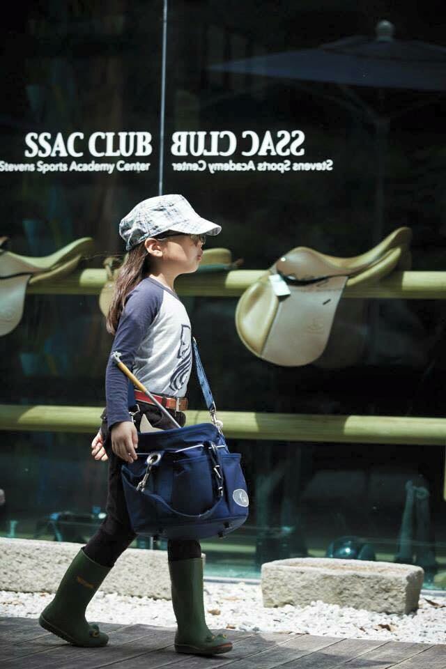 스티븐승마클럽 앞을 마구가 든 가방을 맨 여자아이가 걸어가고 있는 사진
